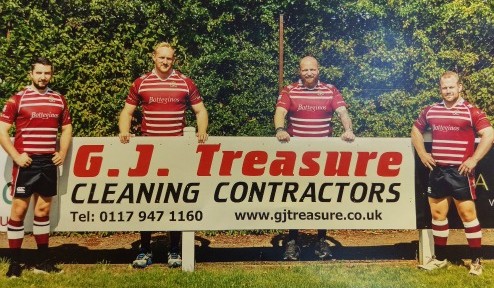 Photo of Cleve Rugby Club Players stood in front of G J Treasure sponsor advertising board